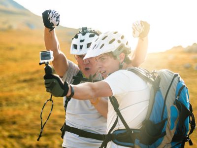 Two men in white sports shirts taking a selfie with a go pro camera on an orange-green meadow.